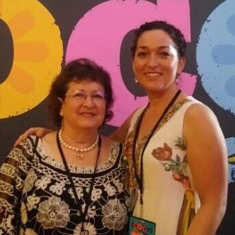 Two women standing next to each other in front of a wall.