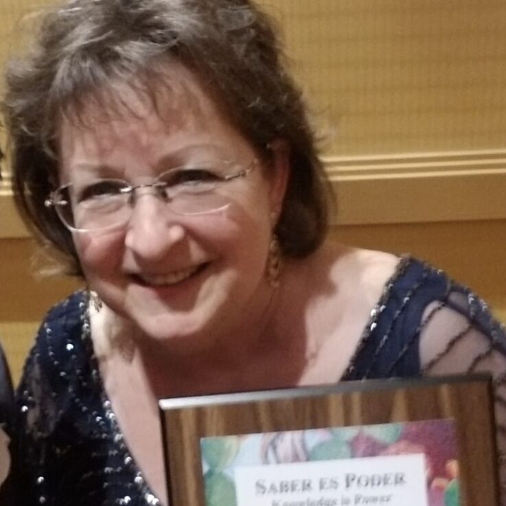 A woman smiling with glasses and holding a plaque.